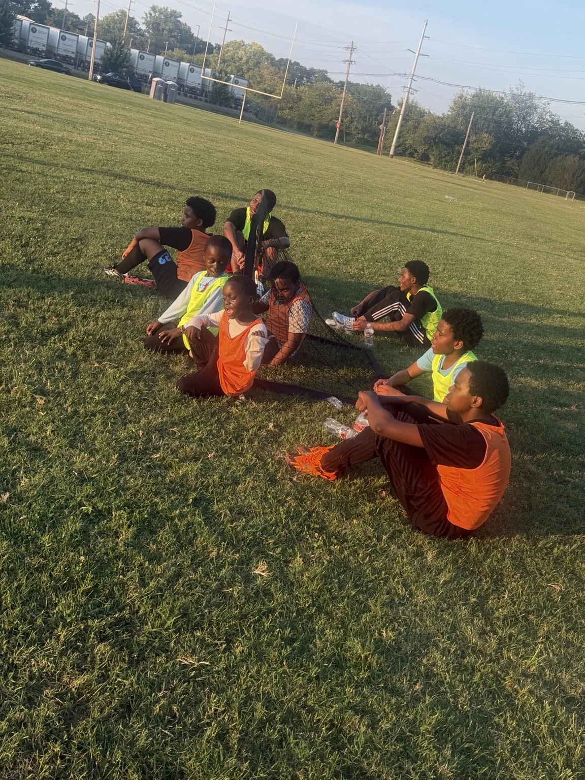 Afrikana United youth resting together beside a small soccer goal during practice