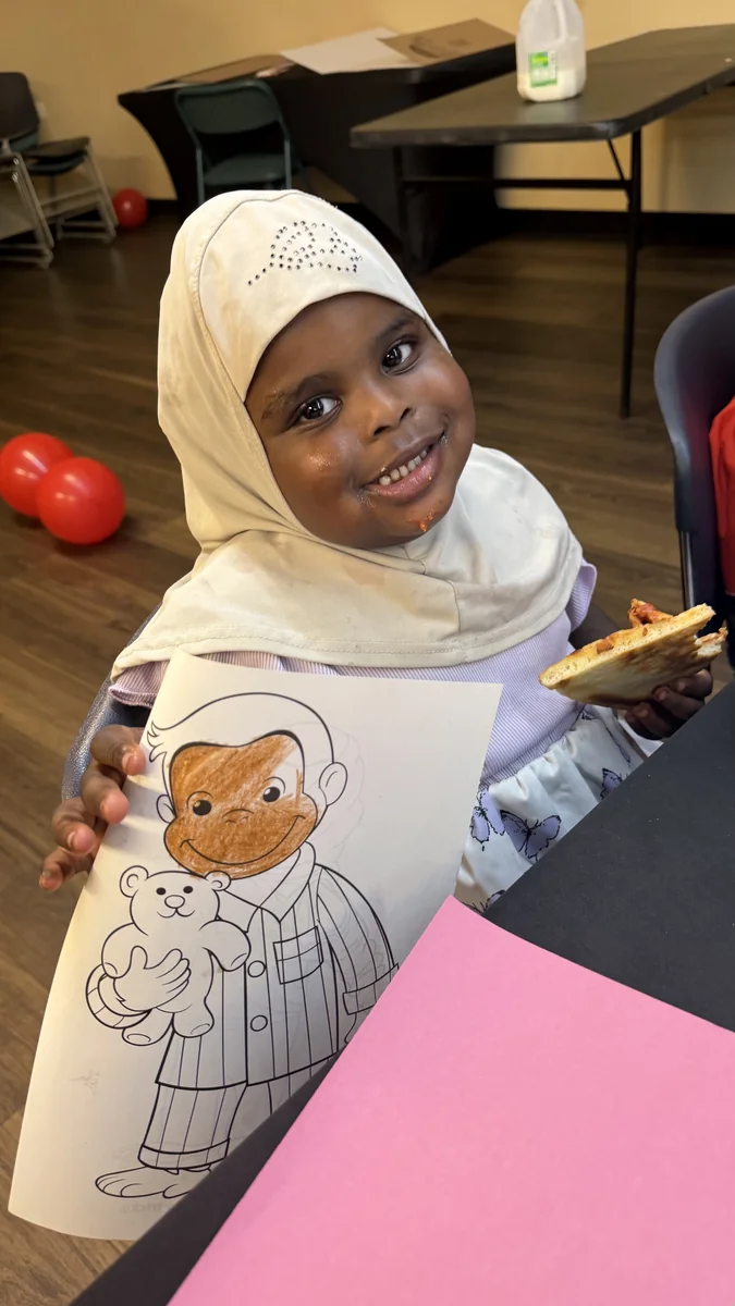 A smiling student proudly shows the artwork she colored.