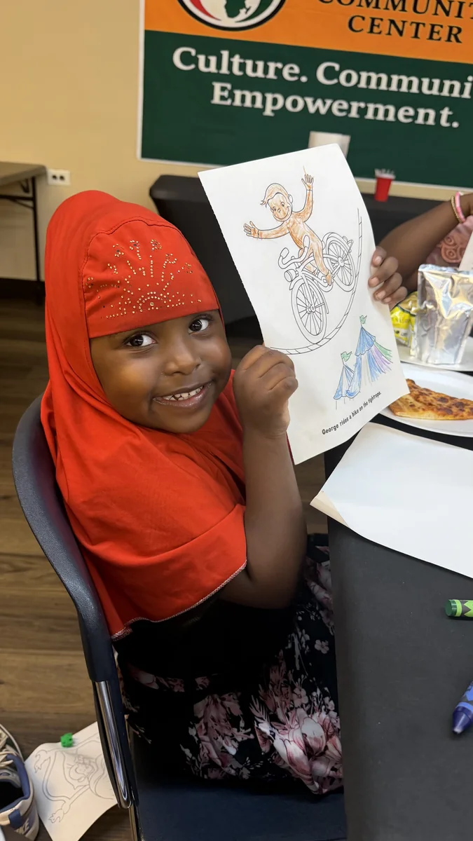 A child beams while holding the picture she colored at the program.